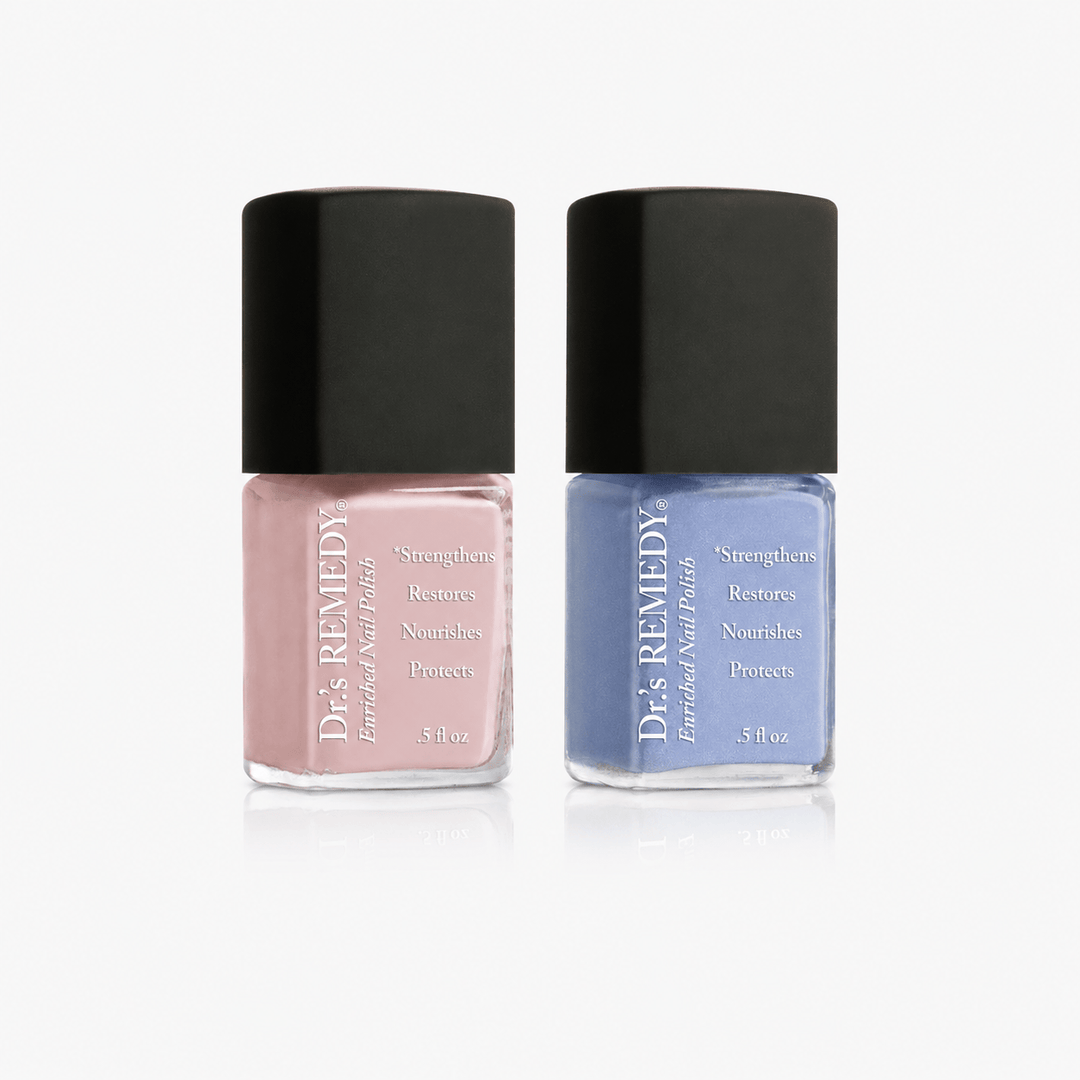 Two bottles of D&K Remedies Enchanted Nail Polish in a pair, featuring one dusty pink polish and one dusty blue polish, both with black caps and clear glass bases on a white background.